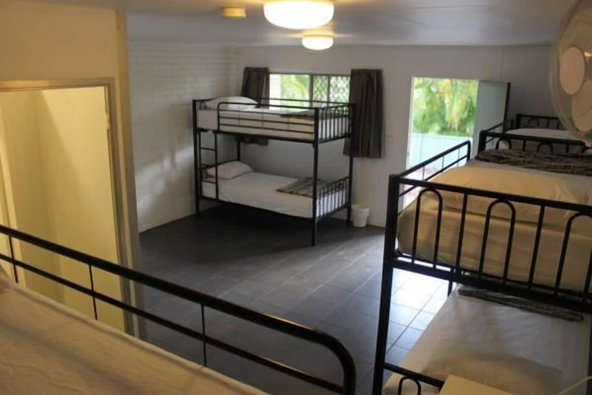 A dormitory room with bunk beds, a window with curtains, and a ceiling fan.