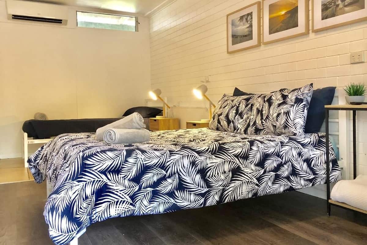 A bedroom with a bed, a bedside table, a lamp, a small plant, and a wall-mounted shelf.