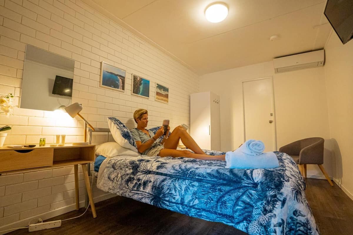 A hotel room with a bed, a desk, a chair, a TV, and a door.