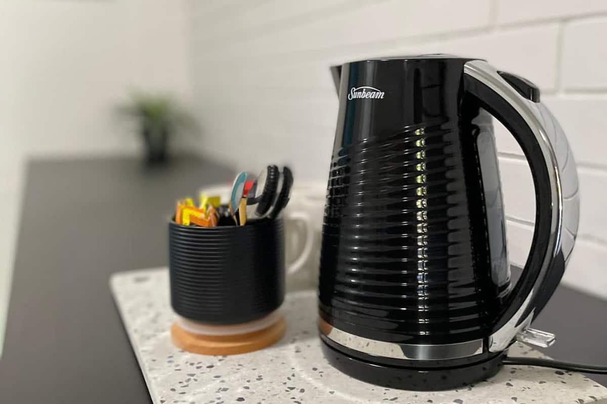 A black Sunbeam electric kettle and a black mug with a wooden coaster on a speckled countertop.