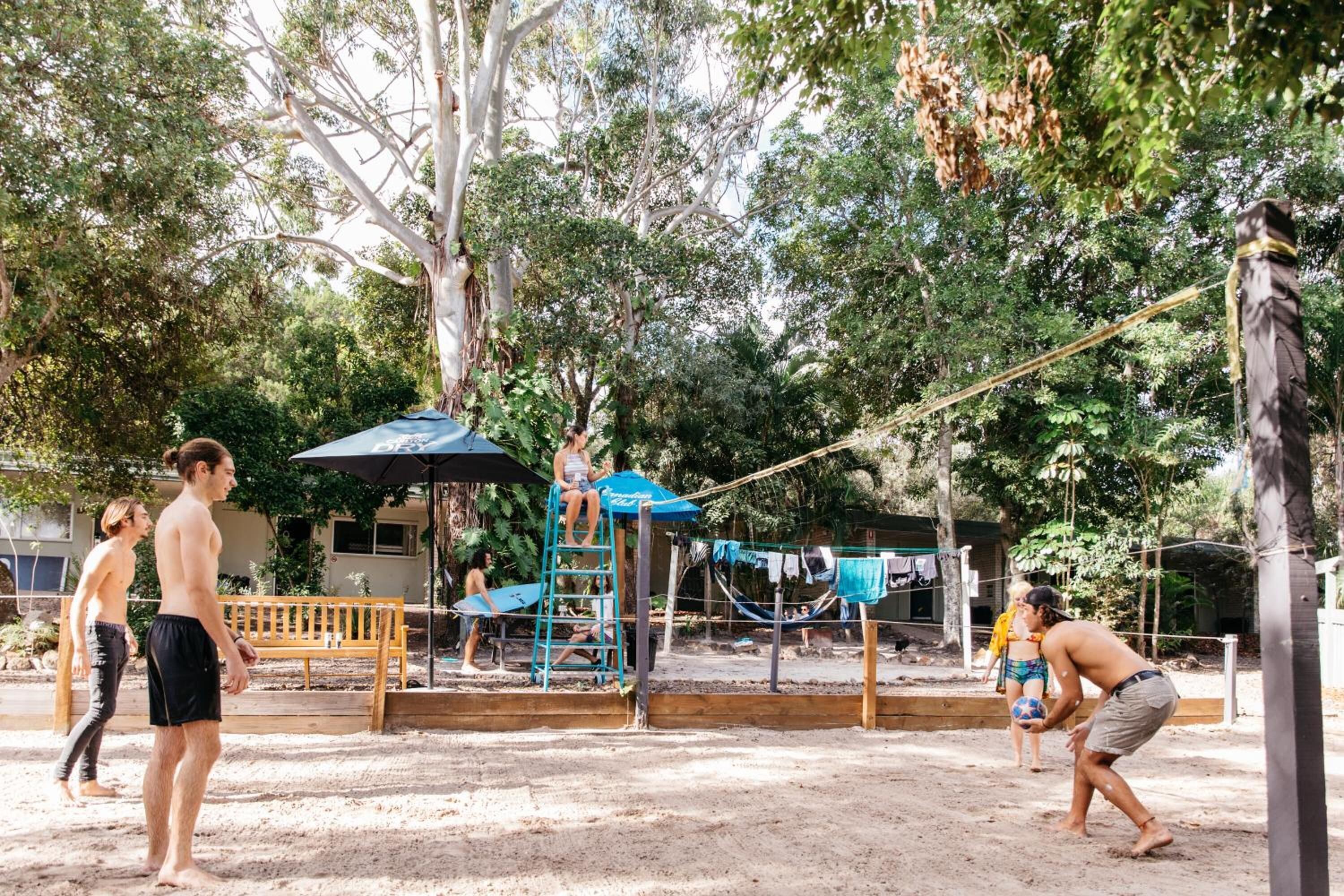 Un espace extérieur sablonneux équipé d’un filet de volley-ball, d’un banc en bois et d’un hamac.