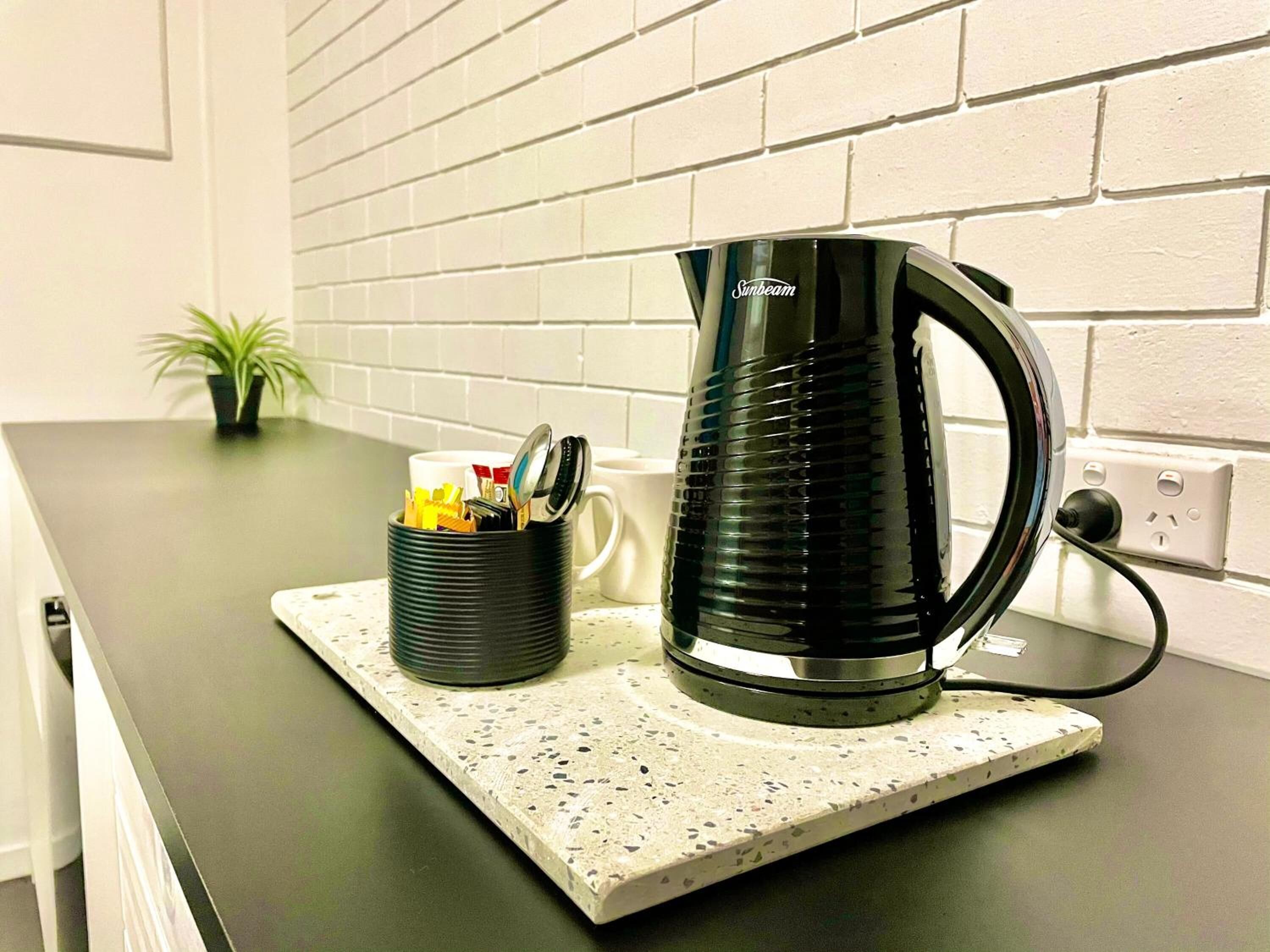 Una encimera de cocina con un hervidor negro, una taza y un recipiente con utensilios.
