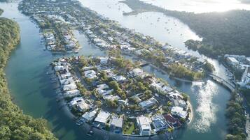 An aerial view of a coastal residential area with houses along the shoreline, a marina with boats, and a bridge connecting the area.