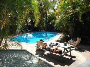 Zona junto a la piscina con piscina, sillas de descanso y una persona recostada en una de ellas.
