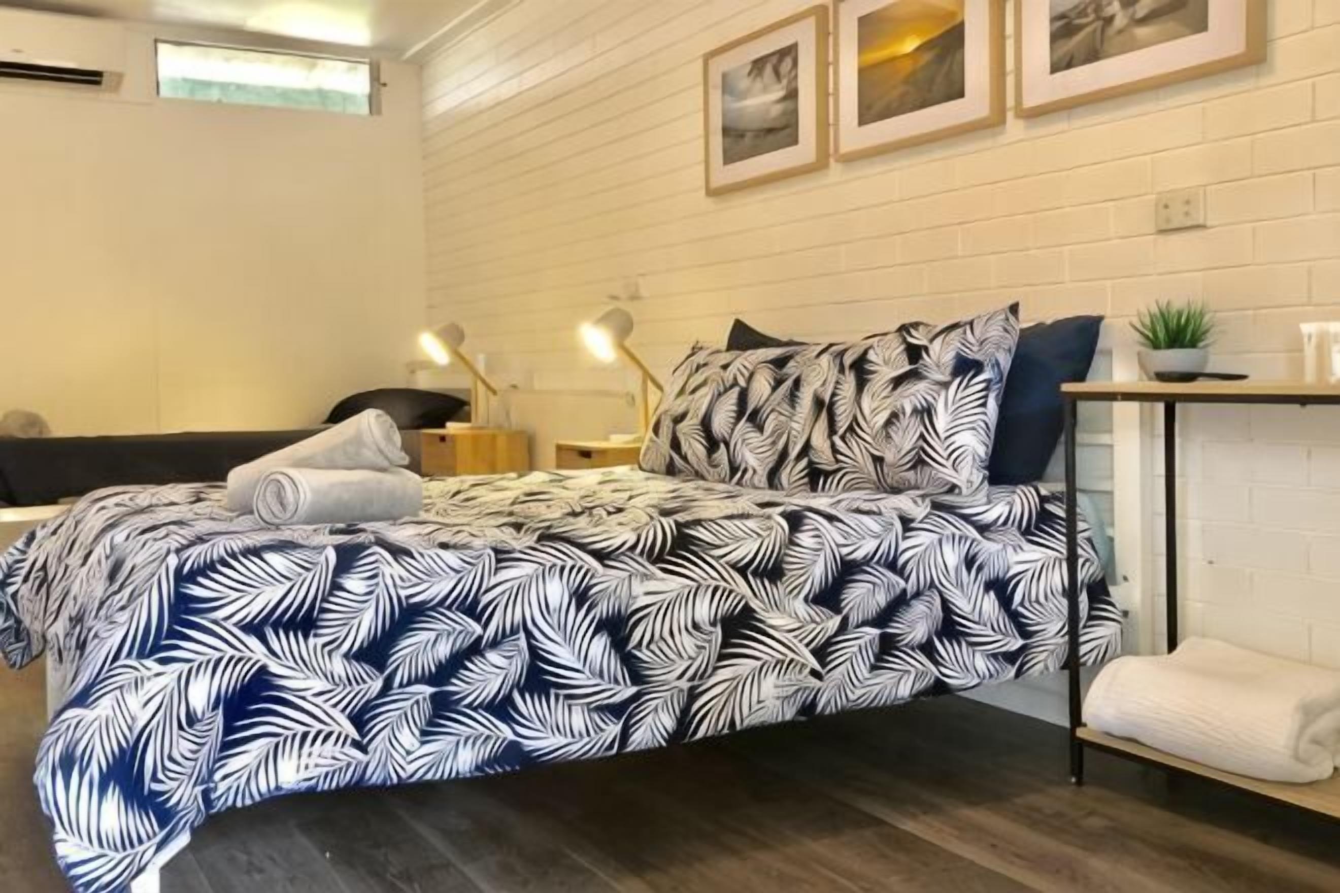 Een netjes opgemaakt slaapkamer met een bed, nachtkastjes, een kleine plant en een wandplank.