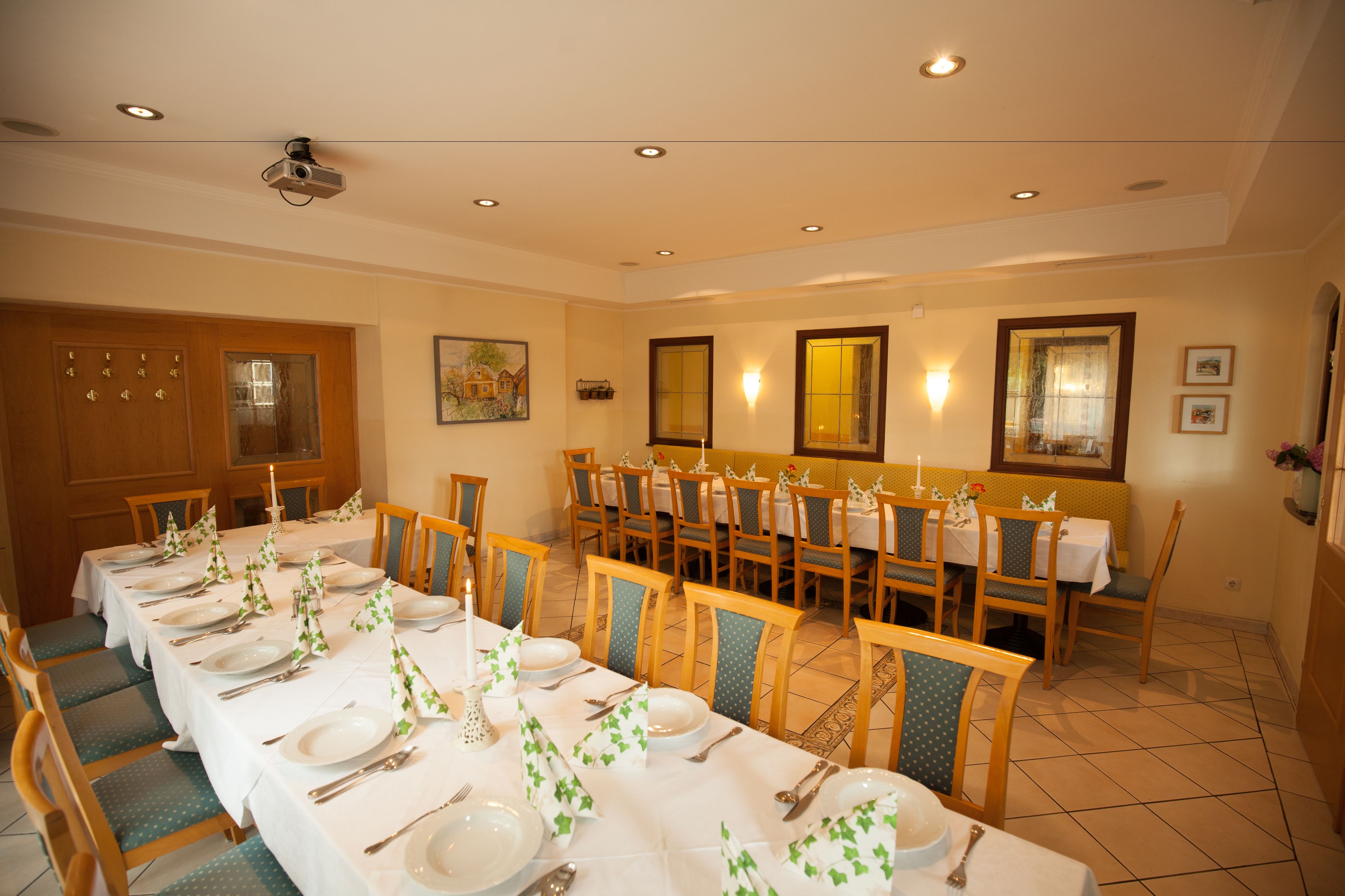 A dining area with multiple tables set for a meal, chairs, and a projector on the ceiling.