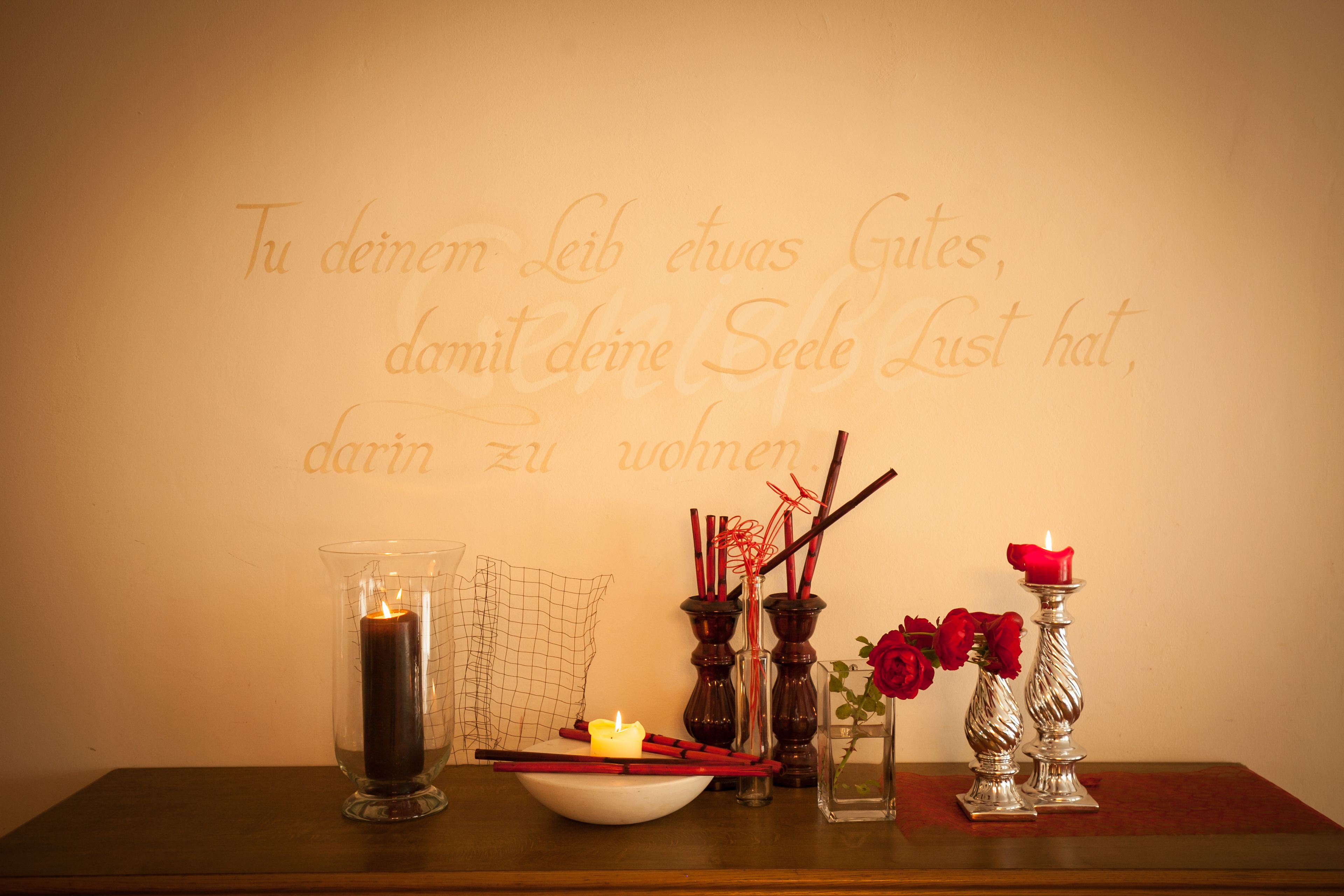 Una mesa con una vela, un cuenco y elementos decorativos, incluyendo rosas rojas y velas en recipientes de vidrio.