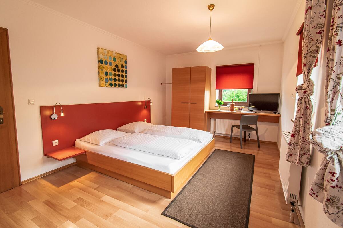 A bedroom with a wooden bed, a desk with a computer, and a window with curtains.