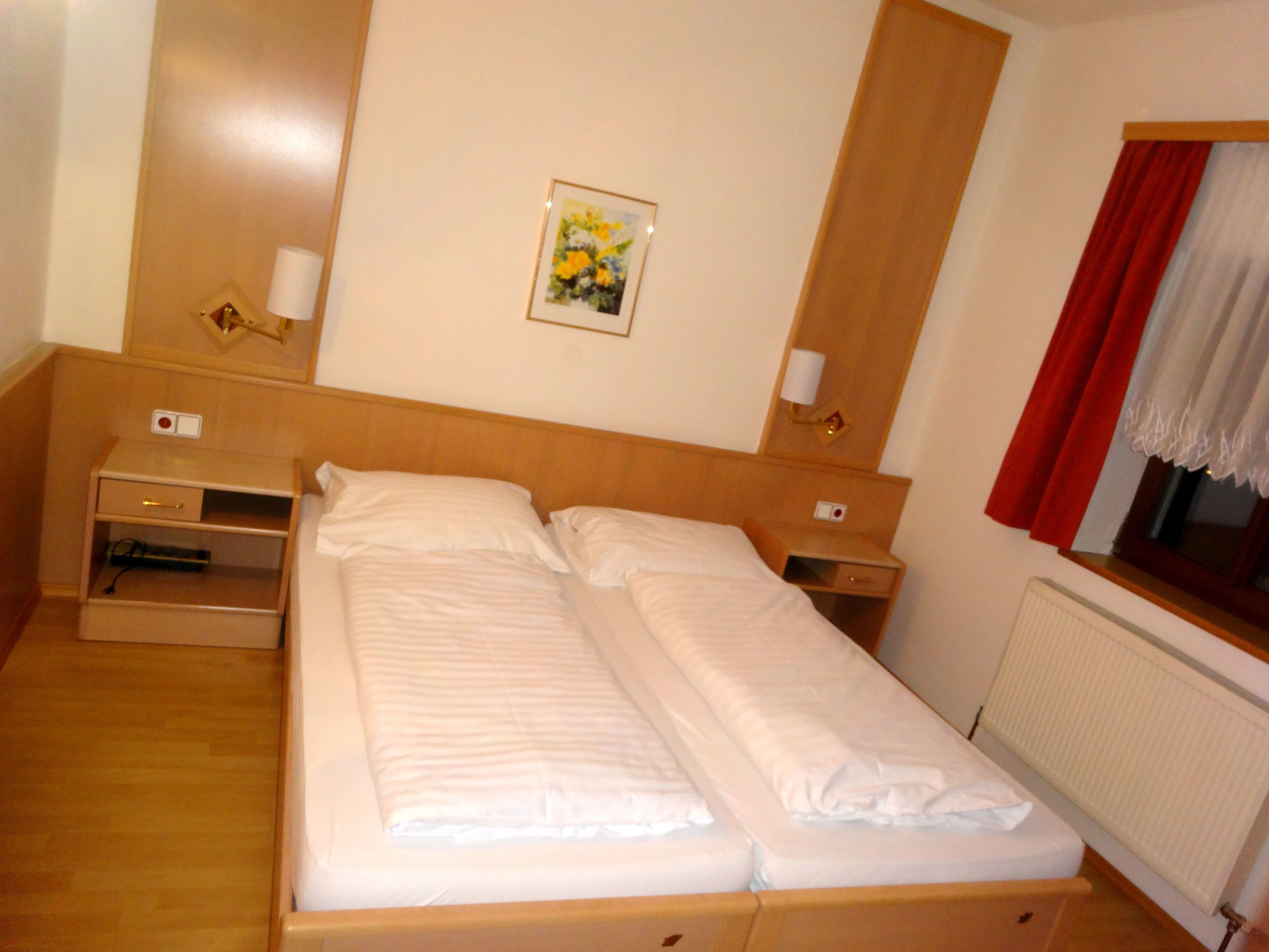 A double bed with a wooden headboard, a bedside table with a lamp, a small shelf, and a framed picture on the wall.