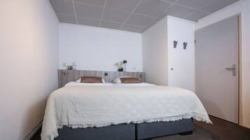 Un dormitorio con cama, mesita de noche, lámpara y puerta.