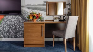 A hotel room with a wooden desk, a grey chair, a TV, a flower vase, and a wind turbine view. - Petit Nord (Hoorn)