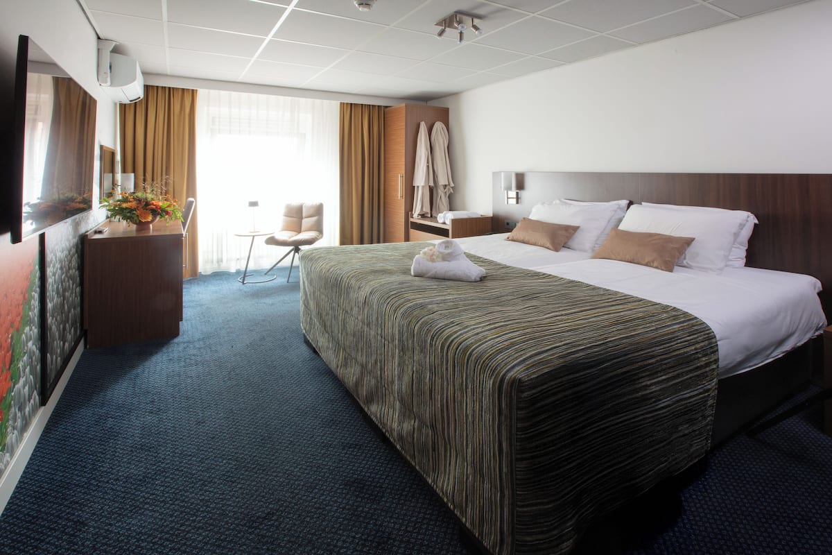 A hotel room with a large bed, a desk, a chair, and a wardrobe.