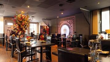 Un restaurant doté de nombreuses tables et chaises, d’un grand arrangement floral en guise de décoration centrale et d’un mur décoratif orné d’un motif circulaire.