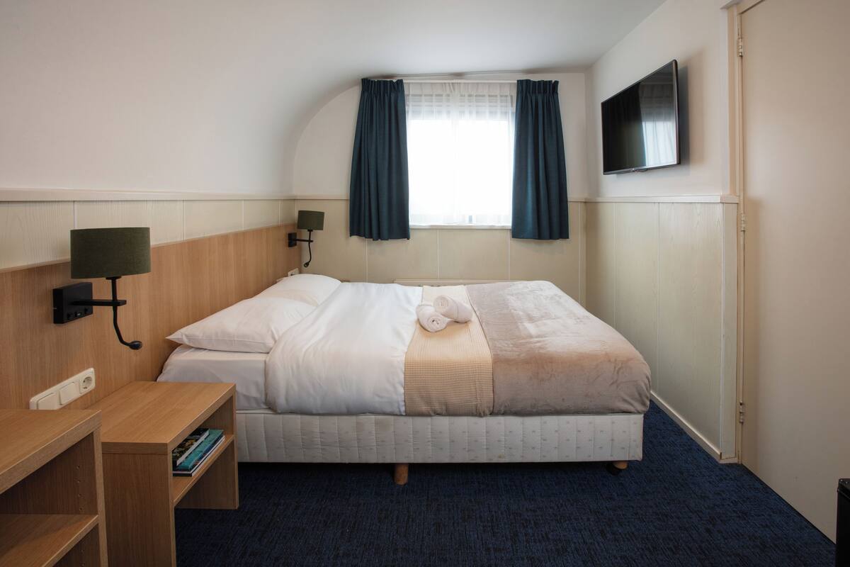 A hotel room with a bed, a desk, a TV, and a window with curtains.