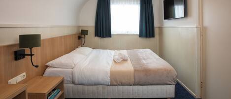 A hotel room with a bed, a desk, a TV, and a window with curtains.
