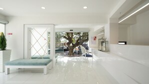 Un vestíbulo limpio y moderno con mostrador de recepción, zona de estar y un gran puerta de vidrio que da a un espacio exterior con un árbol.