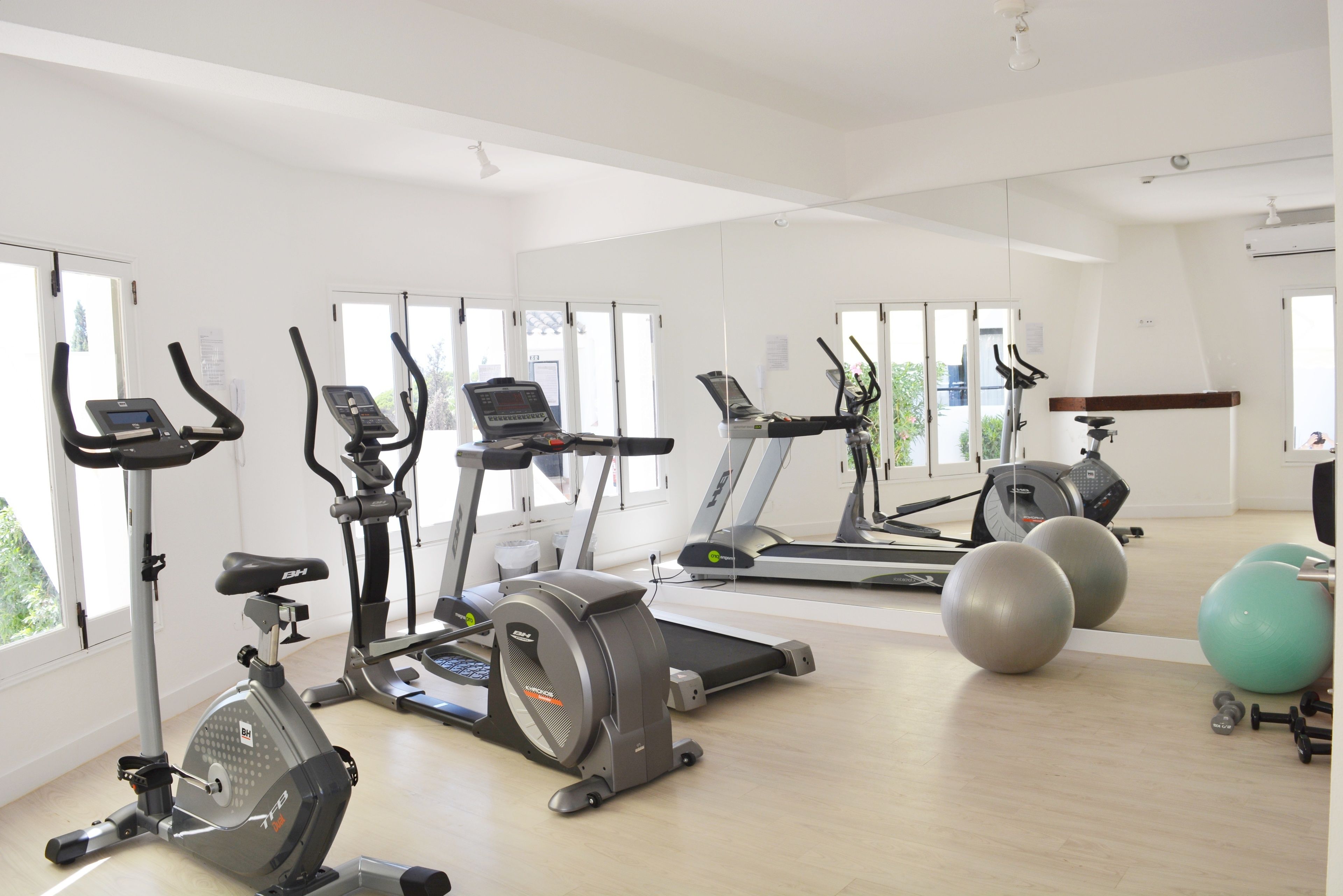 Ein Fitnessstudio mit verschiedenen Trainingsgeräten, darunter Laufbänder, Crosstrainer und Gymbälle.