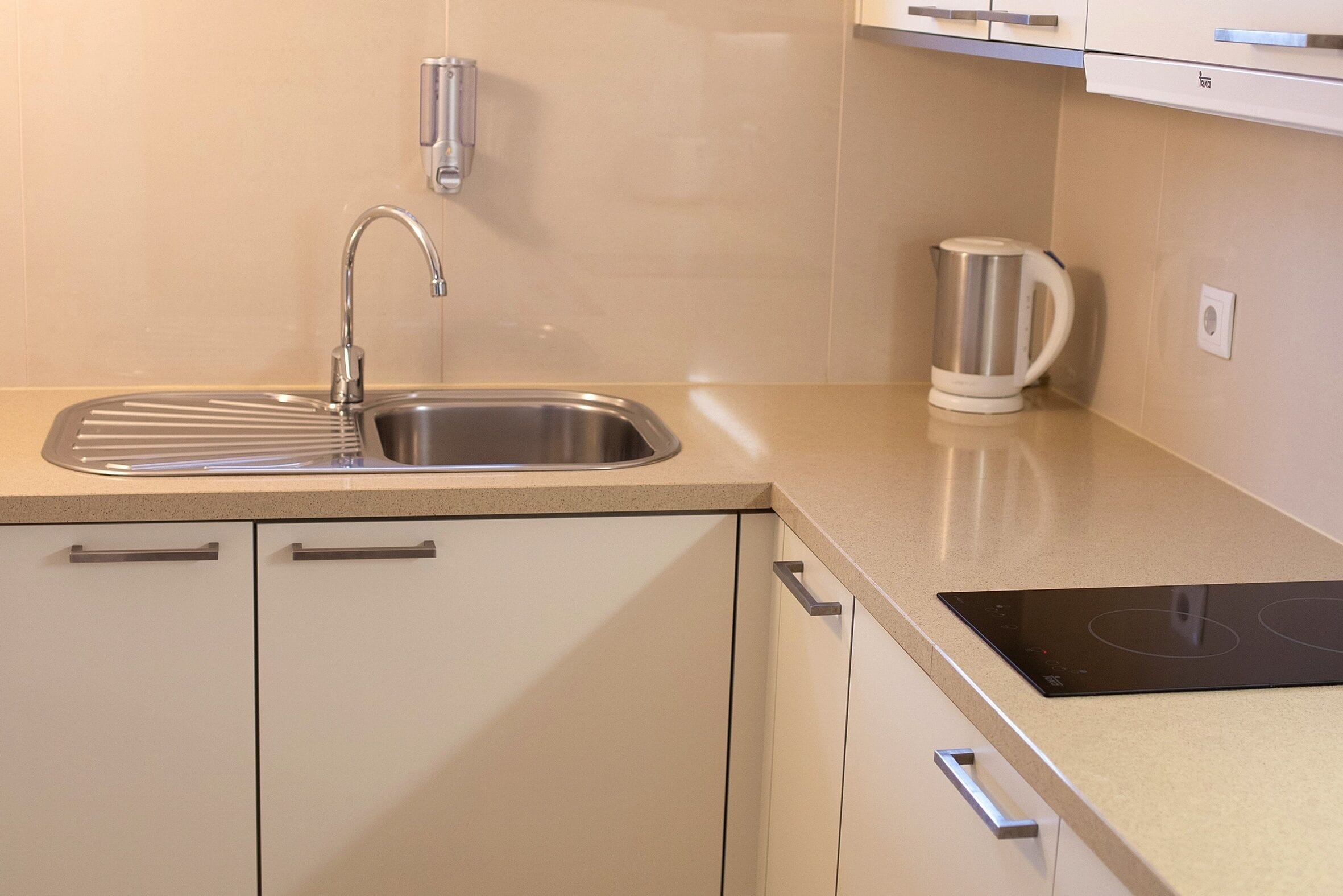 Una cocina con un lavamanos de acero inoxidable, un hervidor y una placa de inducción integrada.