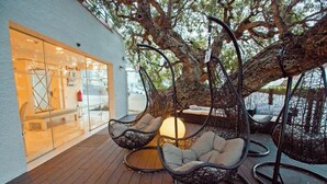 Una terraza de madera con sillas colgantes y una mesa bajo un árbol.