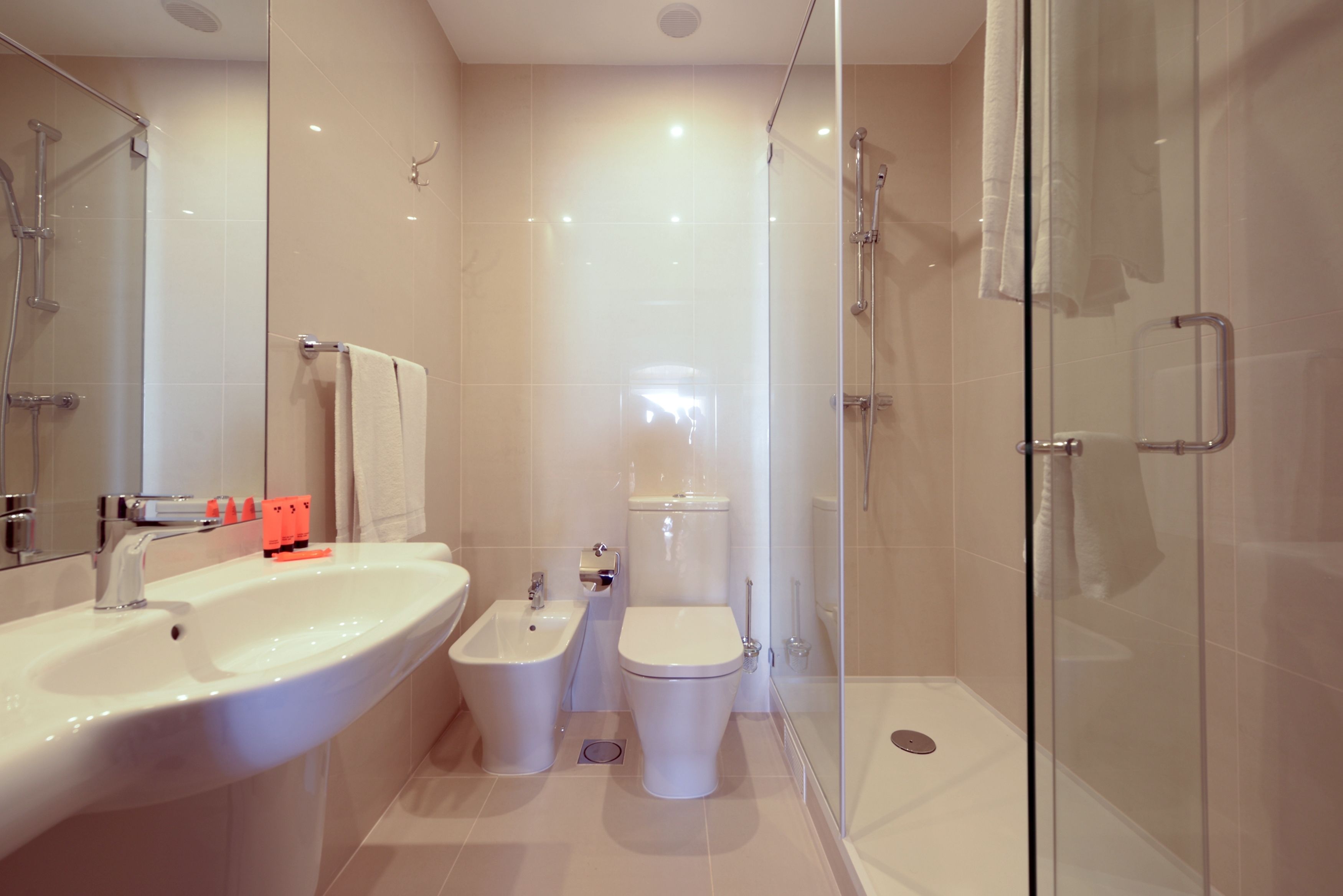 A modern bathroom with a glass shower enclosure, a sink, a bidet, and a toilet.