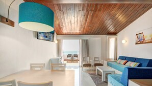 Una sala de estar moderna con techo de madera, un sofá azul, una mesa de comedor con sillas y vistas al exterior.