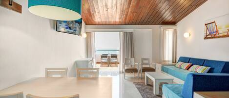 Ein modernes Wohnzimmer mit Holzbalkendecke, einem blauen Sofa, einem Esstisch mit Stühlen und Blick ins Freie.