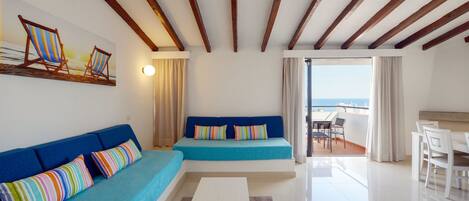 Una sala de estar moderna con un sofá azul, una mesa de centro blanca y vista al mar desde un balcón.