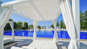 Zona junto a la piscina con sillones blancos y una piscina de agua cristalina.