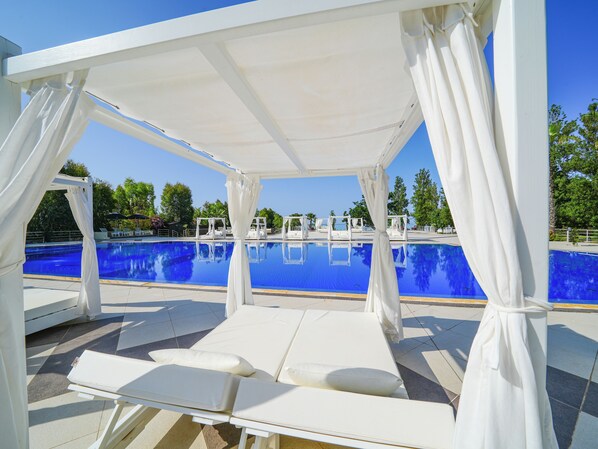 Una piscina al aire libre, sombrillas, sillones reclinables de piscina