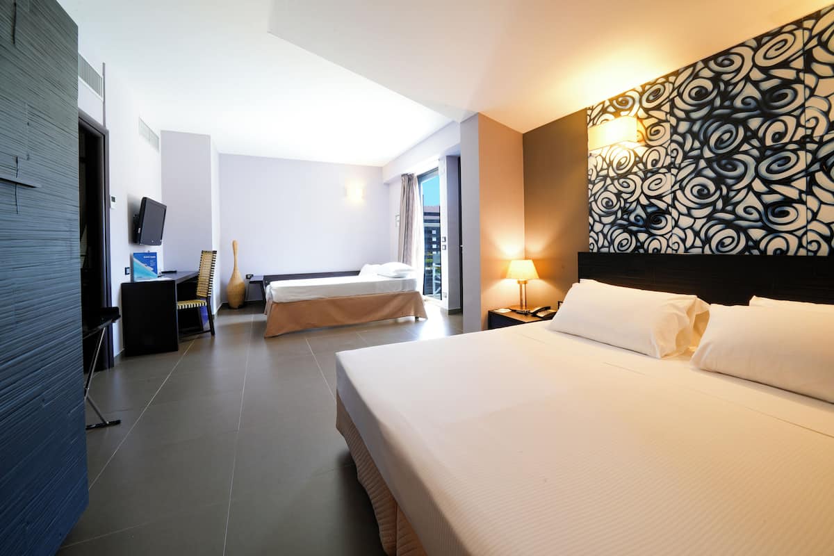 A hotel room with two beds, a TV, a desk, and a patterned wall.