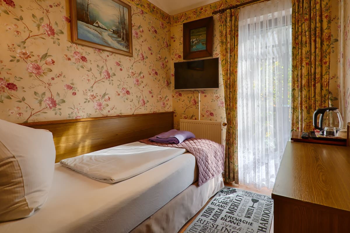 Ein Hotelzimmer mit einem Bett, einem Holzkopfteil, einem an der Wand befestigten Flachbildfernseher, einem Heizkörper und einem Fenster mit Vorhängen.
