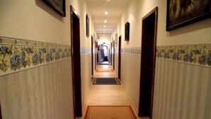 Un couloir d’hôtel avec un sol recouvert de moquette, des portes de chaque côté et une bordure de carreaux le long des murs.