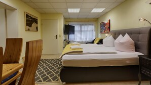 Une chambre d’hôtel avec un lit, des chaises en bois, un bureau, une lampe et des œuvres d’art accrochées aux murs.