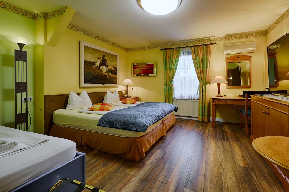 Ein Hotelzimmer mit Bett, Schreibtisch, Stuhl, Lampe, einem Gemälde und einem Fenster mit Vorhängen.