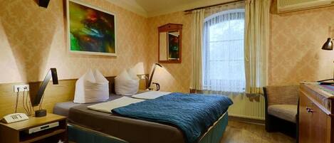 A hotel room with a bed, bedside table, lamp, chair, and a window with curtains.