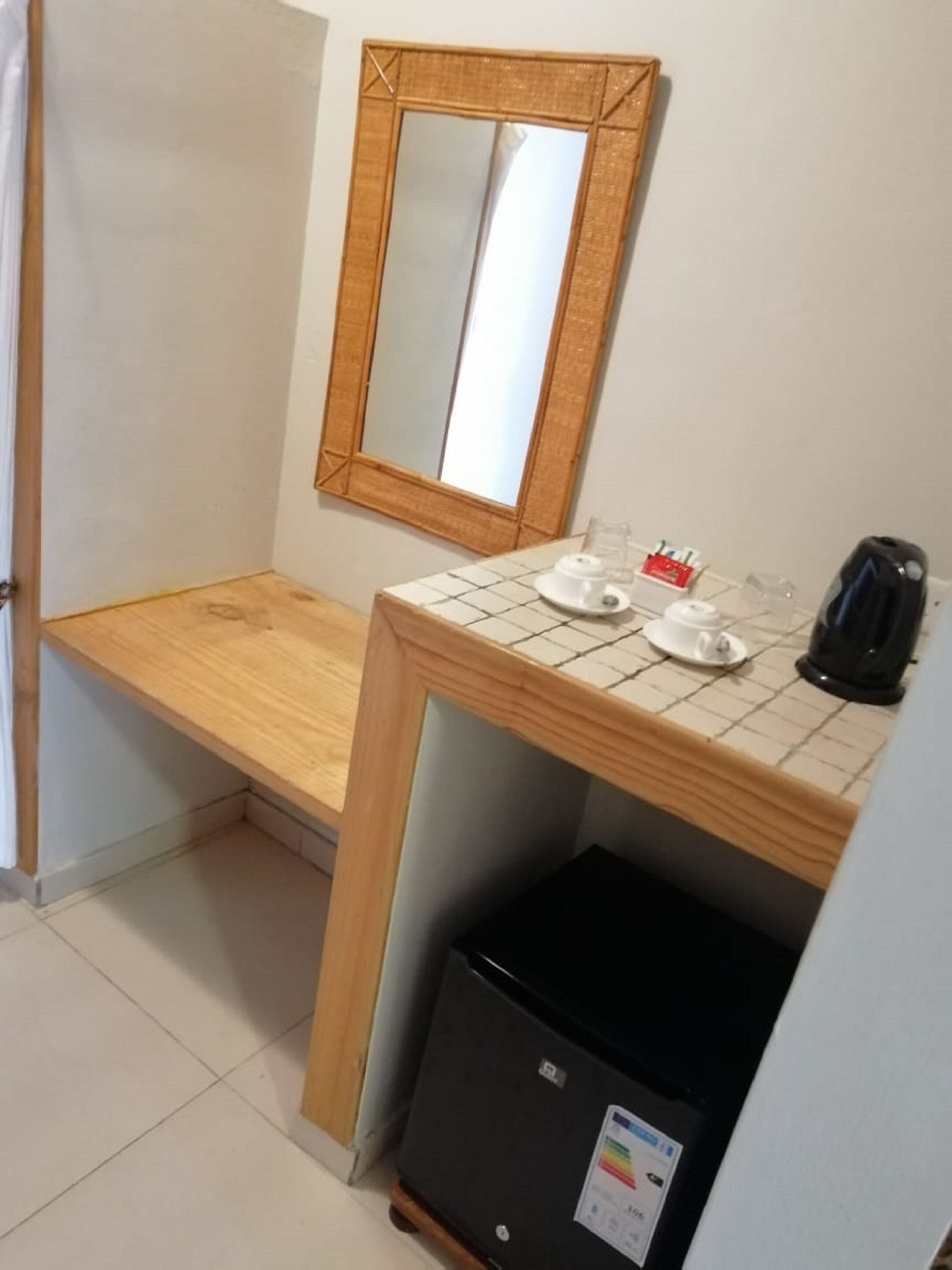 A small kitchenette with a wooden countertop, a mirror, a coffee maker, and a refrigerator.