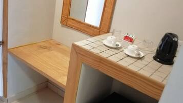 A small kitchenette with a wooden countertop, a mirror, a coffee maker, and a refrigerator.