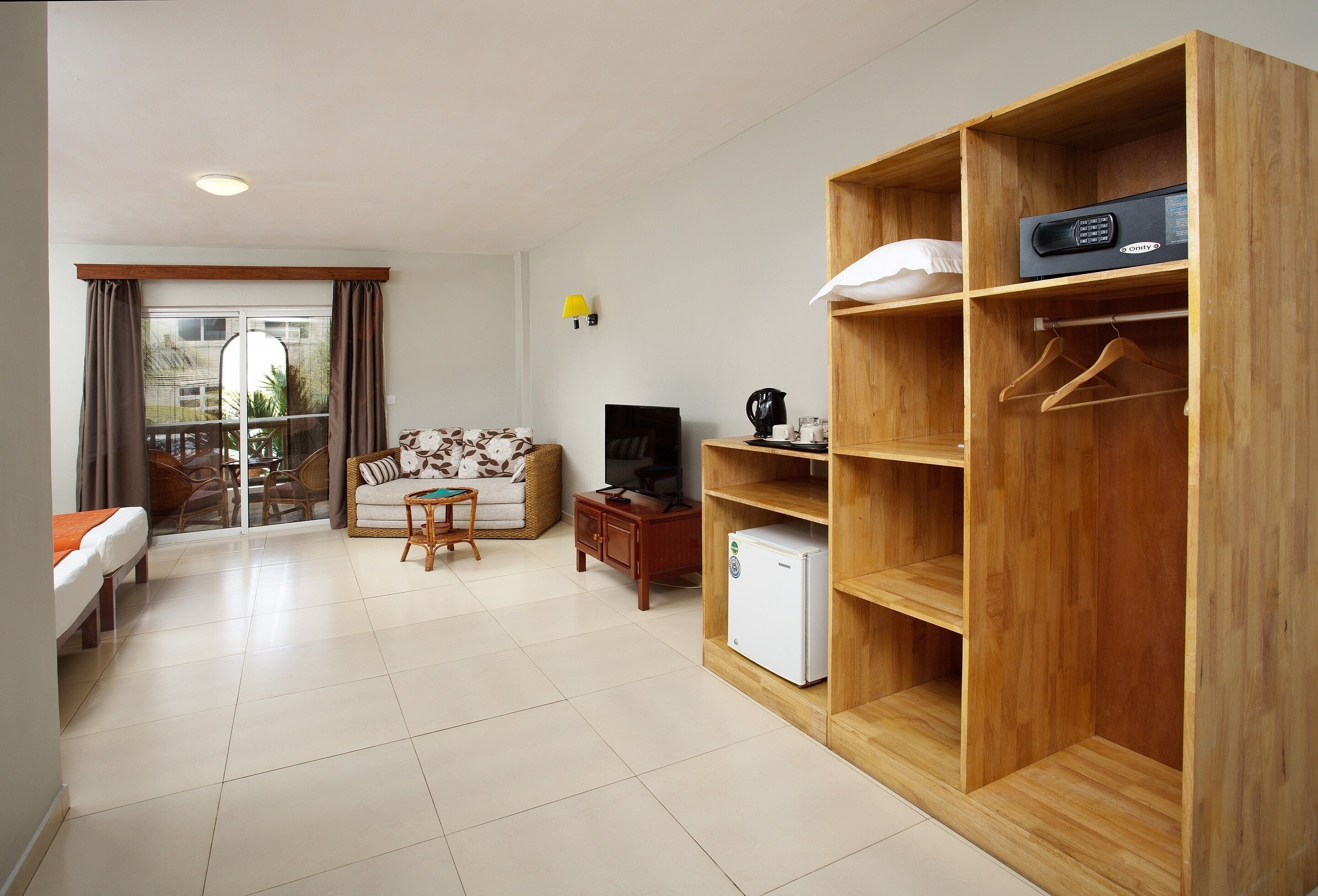 A hotel room with a bed, a sofa, a small table, a TV, a coffee maker, a mini fridge, and a wooden wardrobe with hangers.