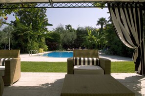 Un espace aménagé au bord de la piscine, avec des meubles en osier, une piscine et une végétation luxuriante.