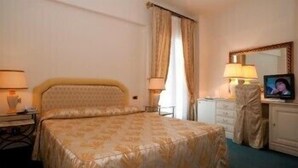 Una habitación de hotel con una cama grande, un escritorio con lámpara, televisión y armario.