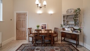 A dining room with a wooden table and chairs, a chandelier, a patterned rug, and a china cabinet with dishes. - The Oratory (Yelverton)