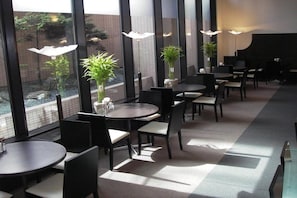 A modern restaurant with round tables and chairs, large windows, and potted plants. - Hotel Sunroute New Sapporo (Sapporo)