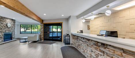 Una zona de recepción con pared de piedra, mostrador de recepción, chimenea y área de estar con sofá y mesa de centro.