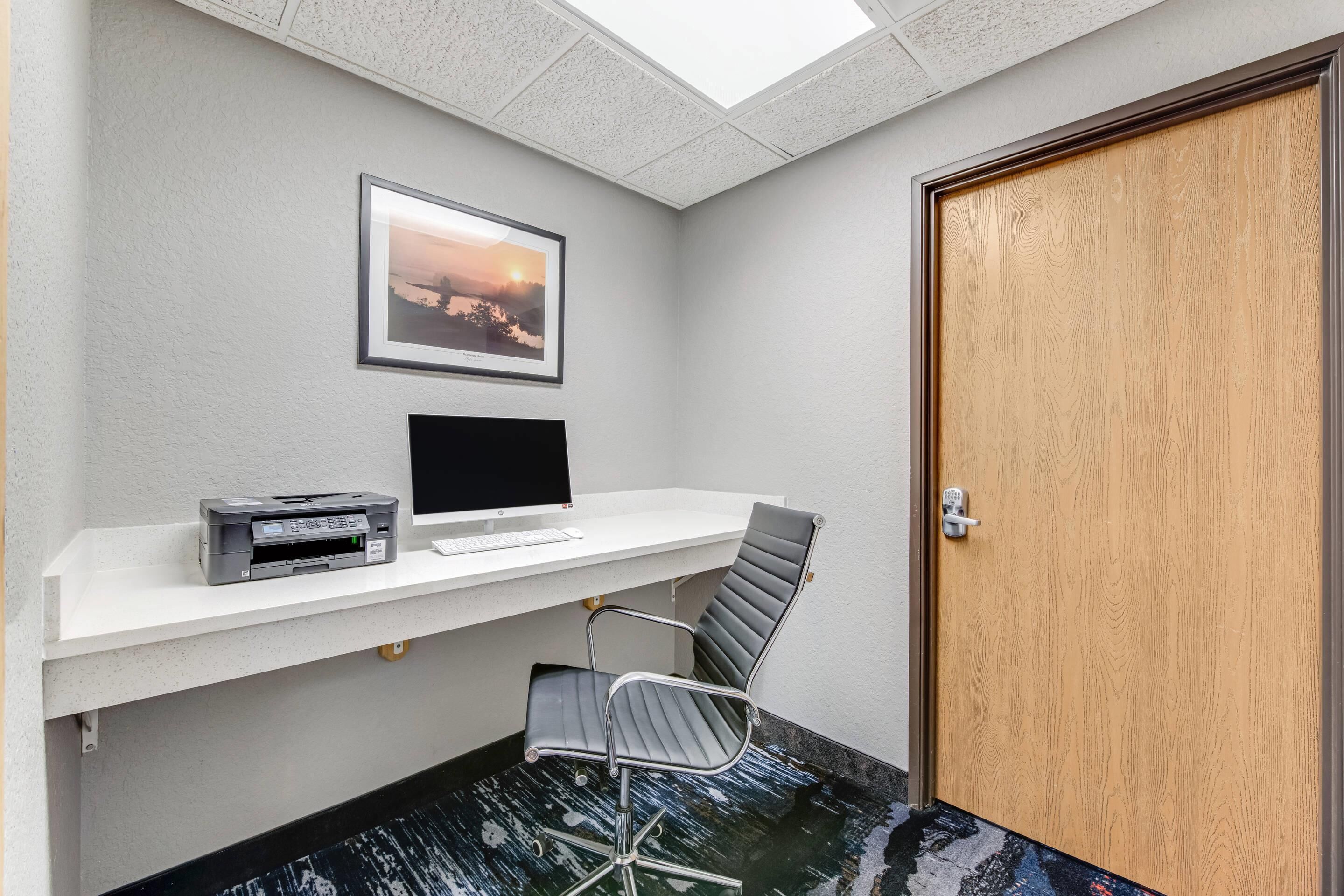 A small office area with a desk, computer, printer, and chair.
