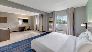 Una habitación de hotel con una cama grande, un escritorio con silla, televisión y ventana con cortinas.