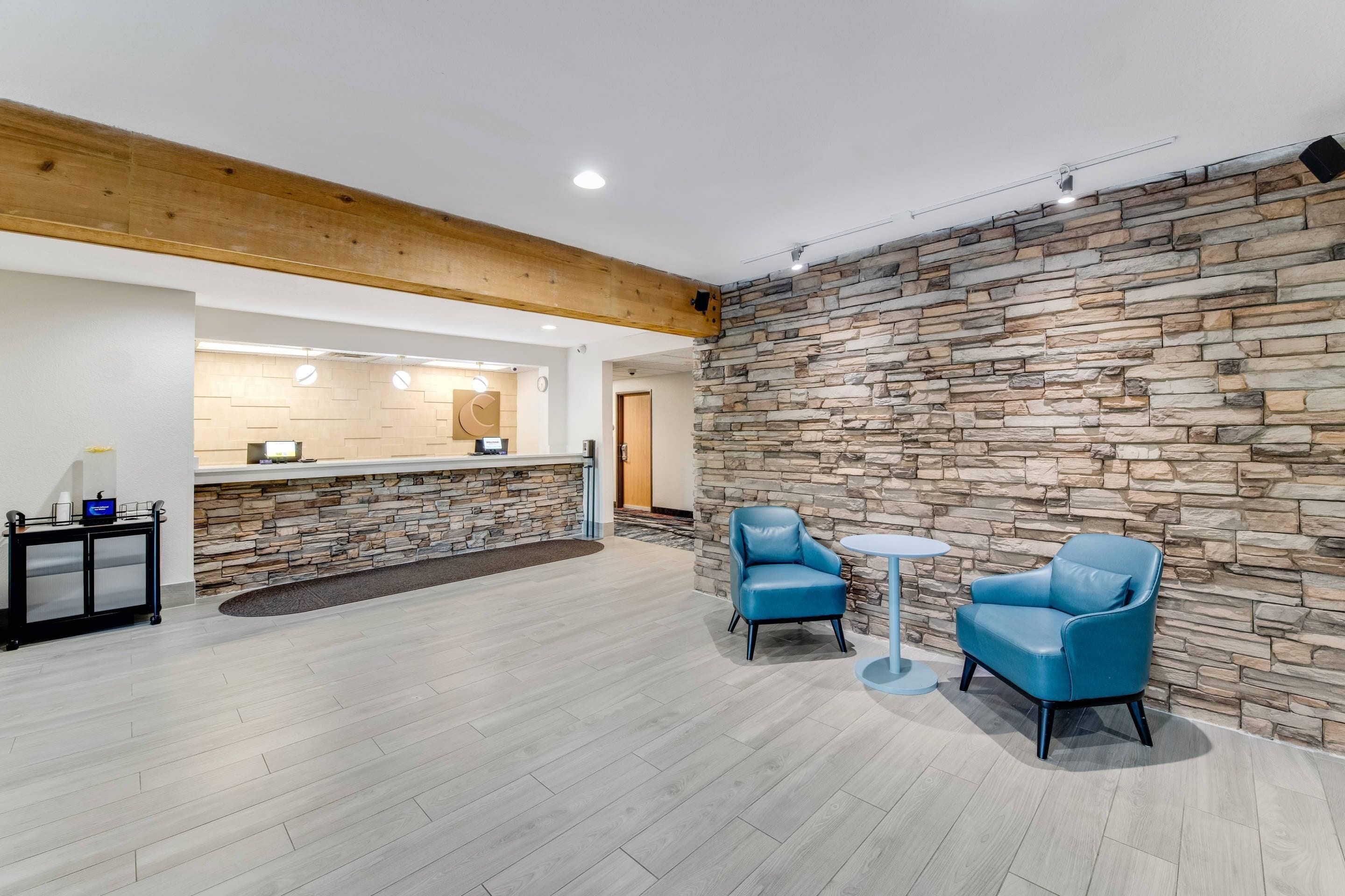 A reception area with a stone wall, wooden ceiling beams, and a reception desk. There are two blue chairs and a small round table.