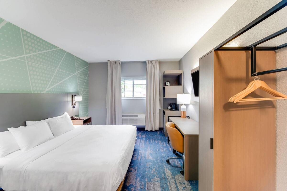 Habitación de hotel con cama, escritorio, silla y un perchero de madera.