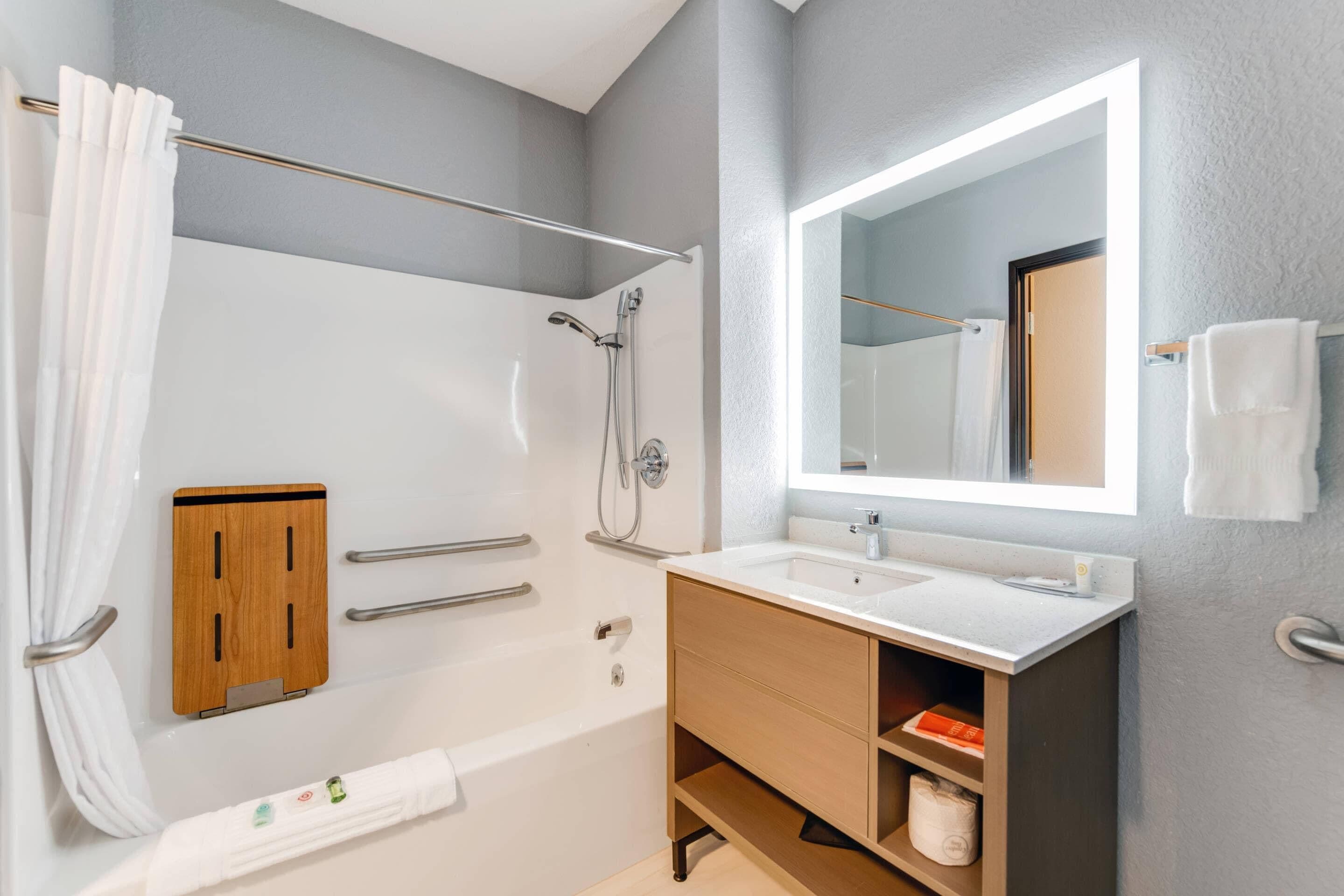 A modern bathroom with a bathtub, shower, vanity, and a large mirror.