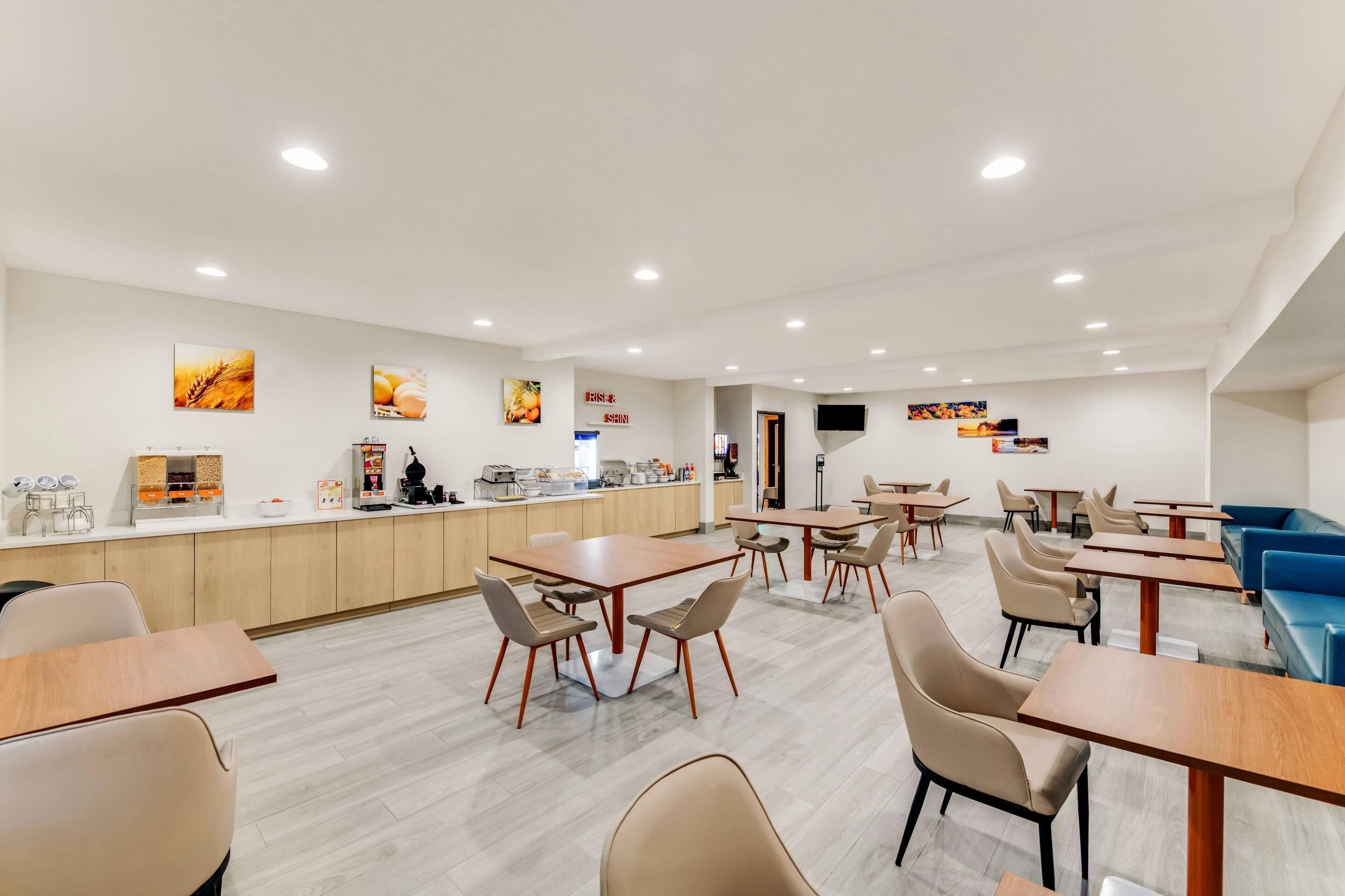 Un comedor moderno con mesas y sillas de madera, una barra con alimentos y un televisor montado en la pared.