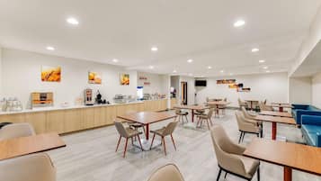 Un comedor moderno con mesas y sillas de madera, una barra con alimentos y un televisor montado en la pared.